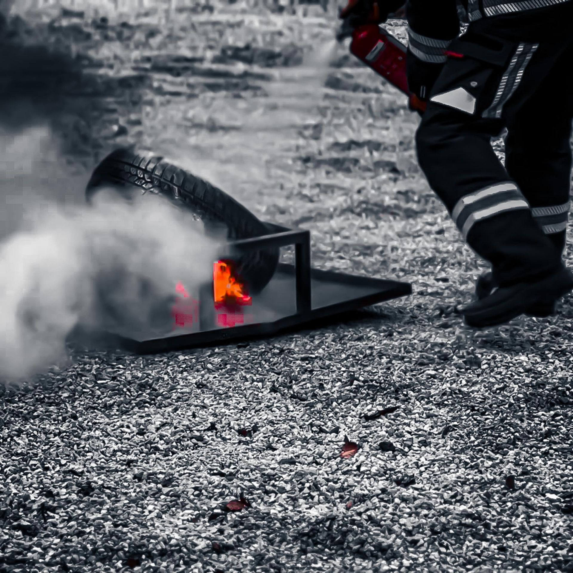 Een brandweerman blust een brandende band op een metalen bak, waarbij dikke rookwolken opstijgen.
