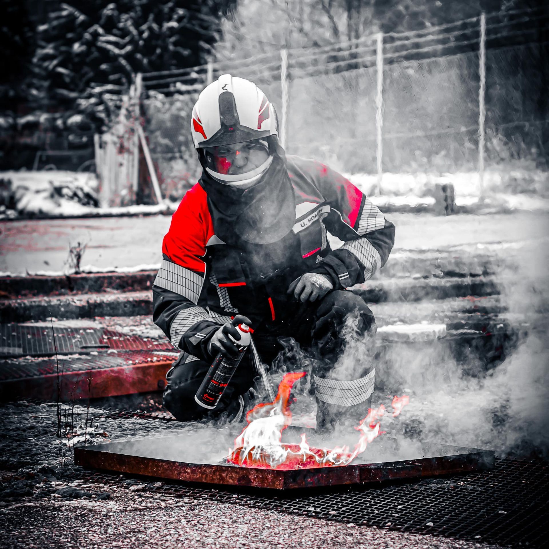 Brandweerman blust een brand in een metalen bak in de buitenlucht. Rood-wit pak, besneeuwde achtergrond.