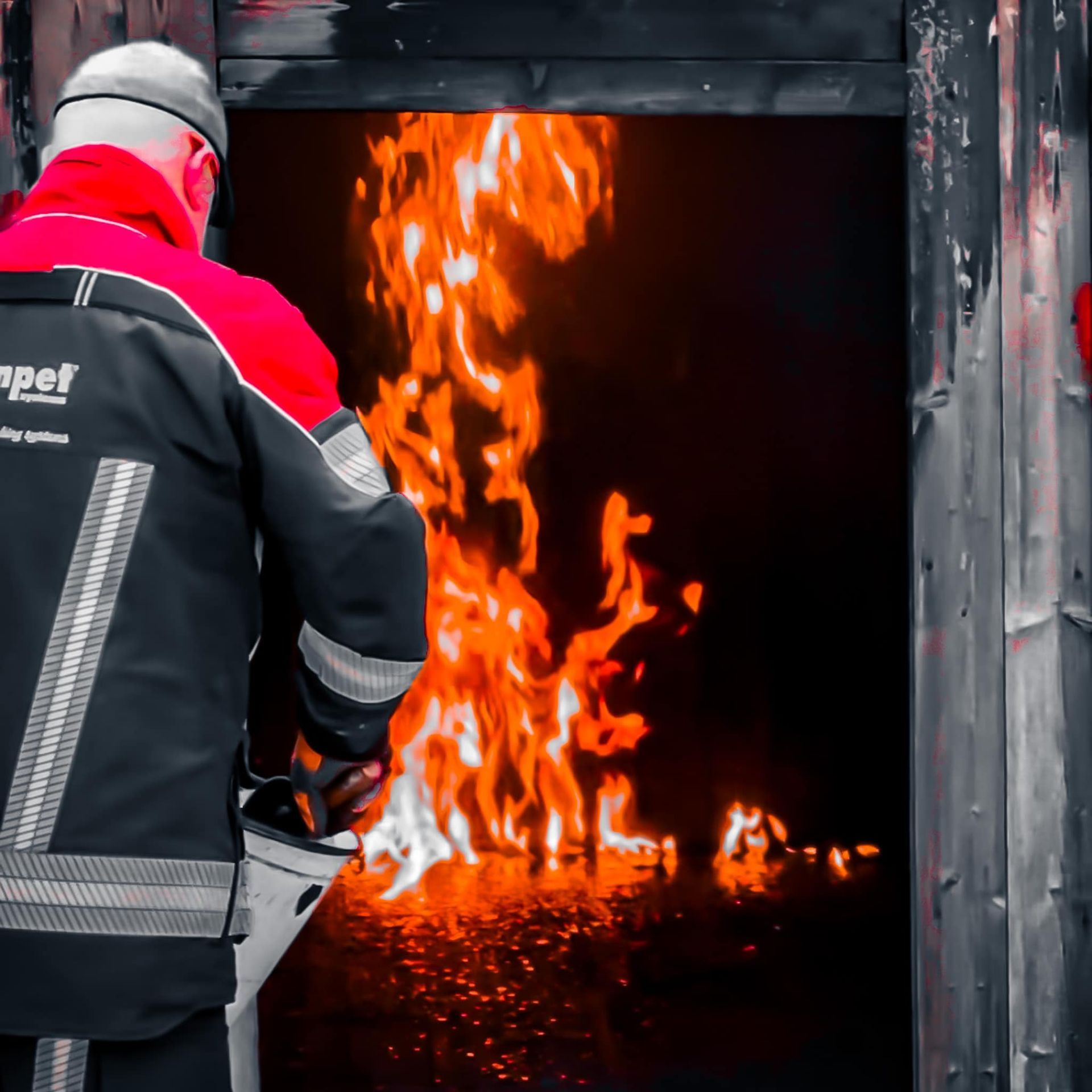 Brandweerman in beschermende kleding die vanuit een deuropening de vlammen trotseert.