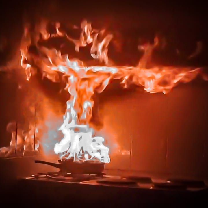 In een donkere keuken schieten vlammen uit een pan op het fornuis, wat een vurige explosie veroorzaakt.