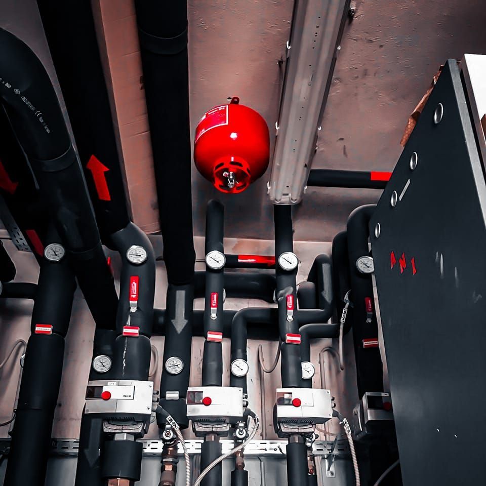 Rood brandblussysteem in een technische ruimte met zwarte leidingen en meters.