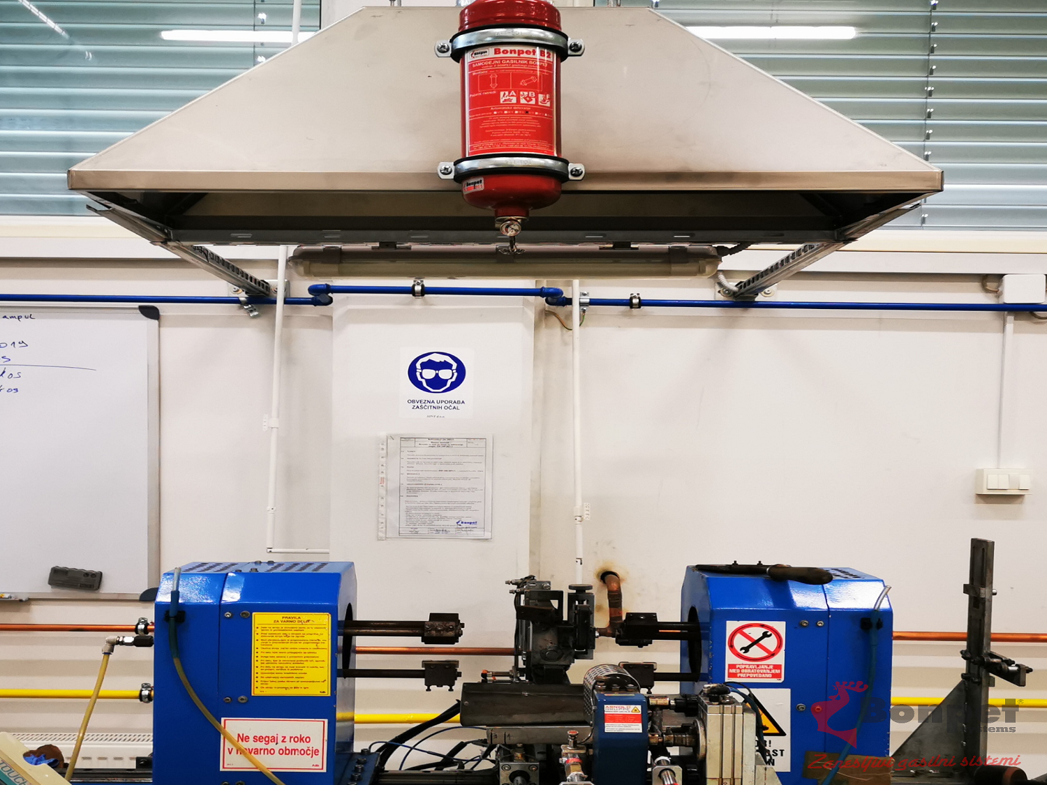 Machine met rode brandblusser erboven, blauwe onderdelen en waarschuwingsbord.