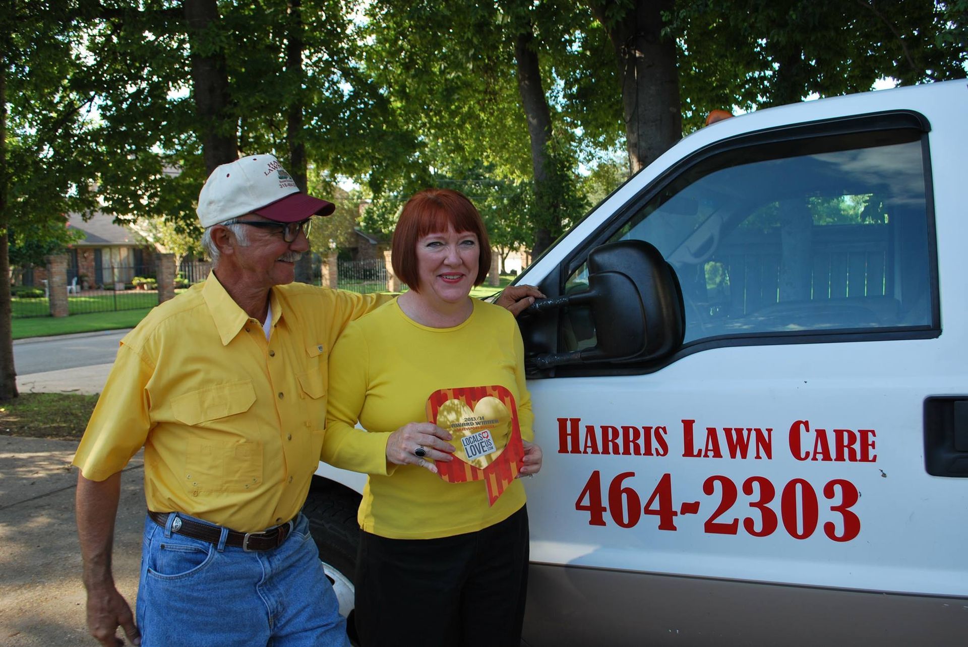 Two people standing beside a white Harris Lawn Care van with red lettering and phone number 464-2303.