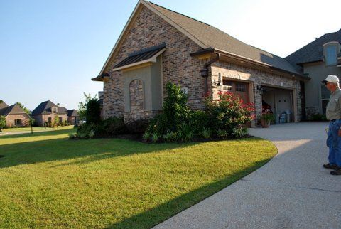 Brick suburban house with a manicured lawn, driveway, and a person standing near the garage.