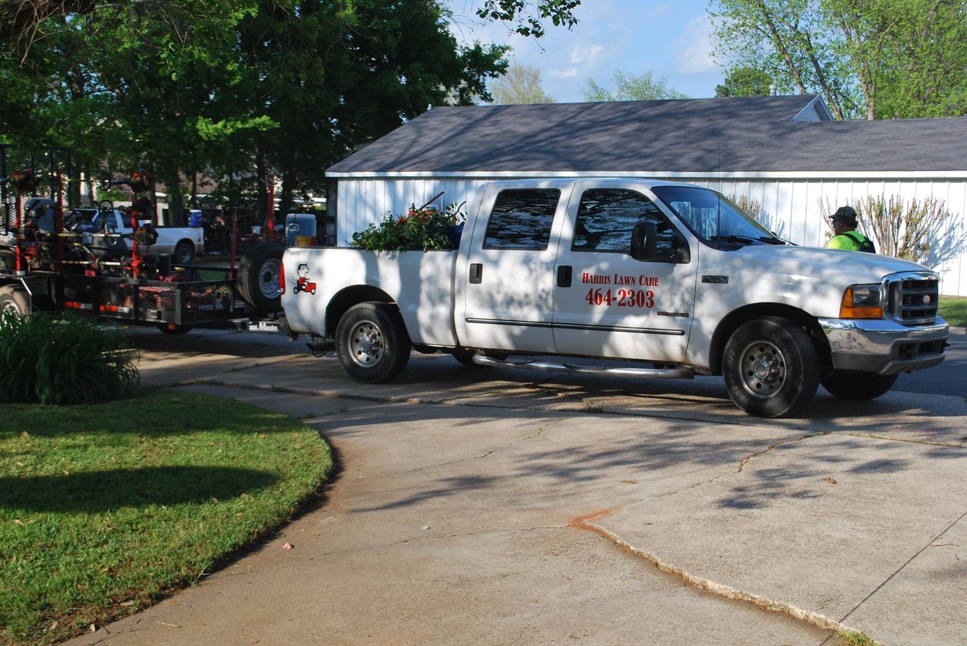 White utility truck parked in a driveway beside a fire engine, with trees and a house in the background