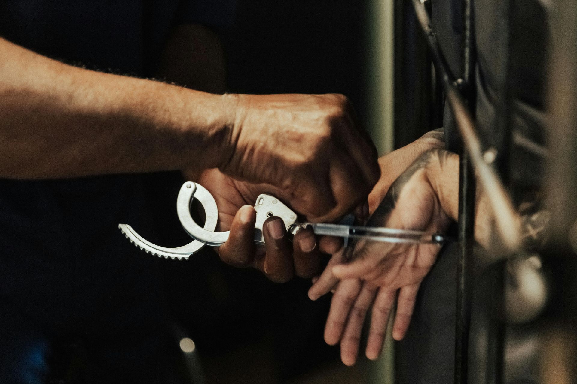 Person being handcuffed inside a jail cell, with the hand of a person applying the cuffs.