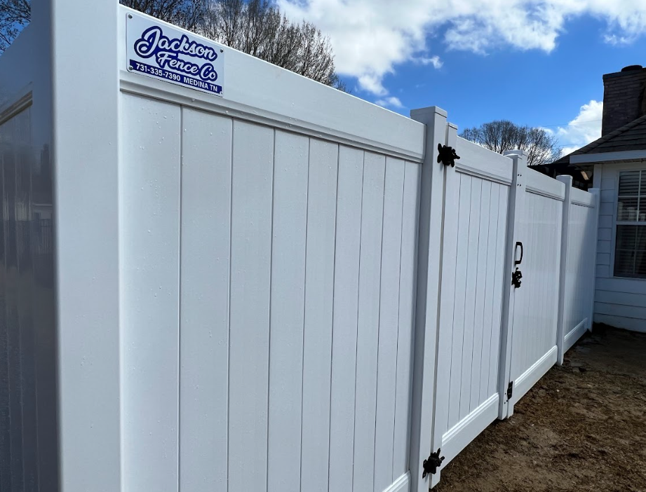 White vinyl fence with gate beside a house, with a blue-and-white sign on the left panel.