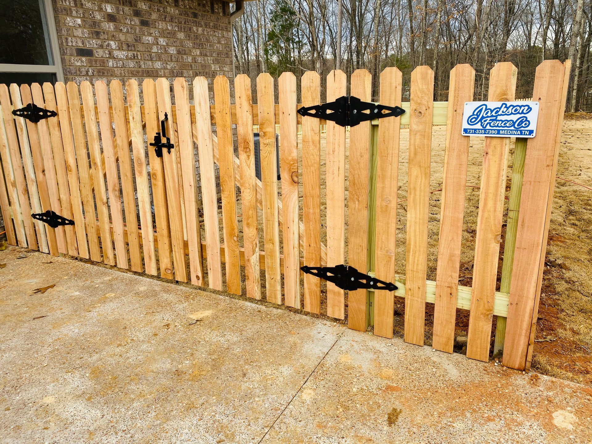Wooden fence gate with black hinges and blue sign beside a concrete driveway