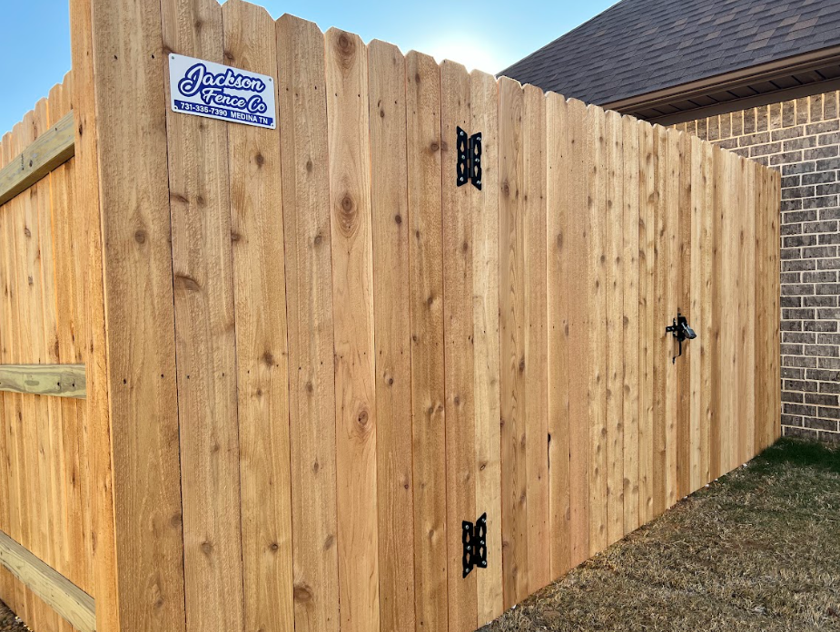 Wooden backyard gate and privacy fence with black hinges beside a brick house