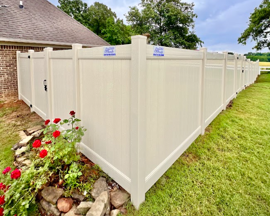 White vinyl privacy fence enclosing a green yard beside a brick house, with flowers in the corner.