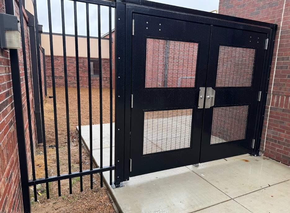 Black metal gate and fence beside a concrete walkway at a brick building entrance
