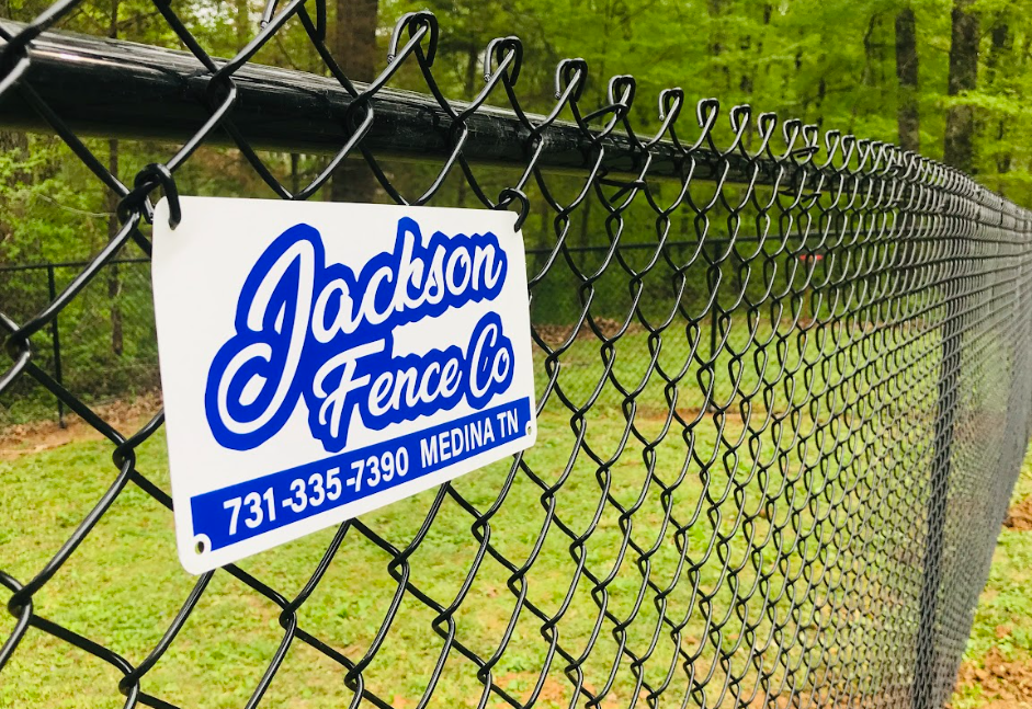Jackson Fence Co. sign on a black chain-link fence in a green wooded area