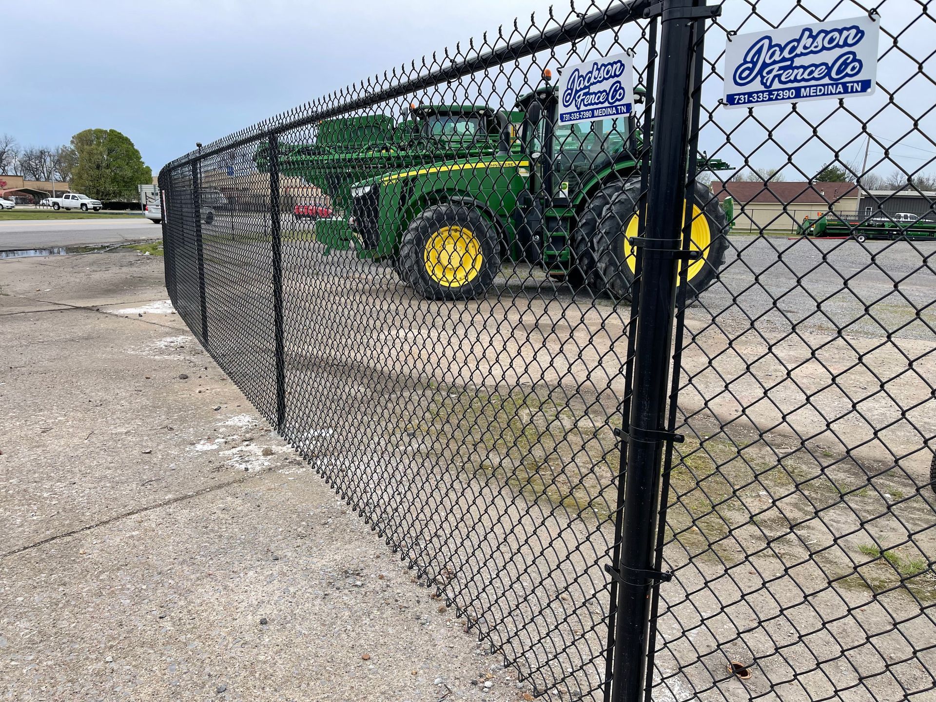 Green tractor parked behind a chain-link fence on a paved lot near a sign.