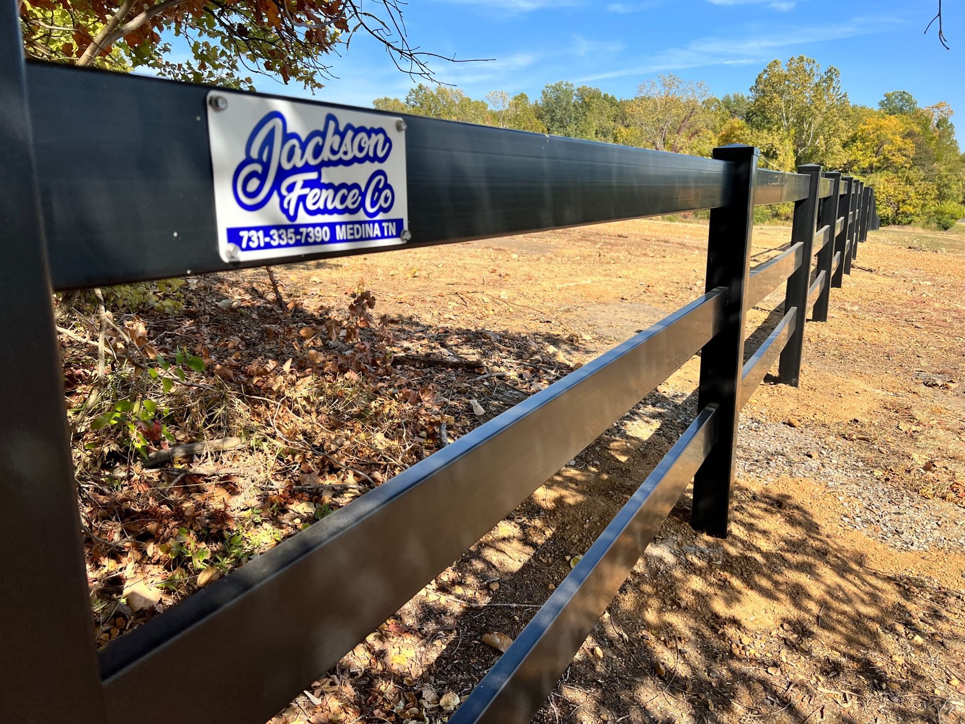Black fence with a Jackson Farm sign along a dirt roadside in a rural field