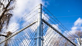 Chain-link fence corner with metal posts against a blue sky with clouds