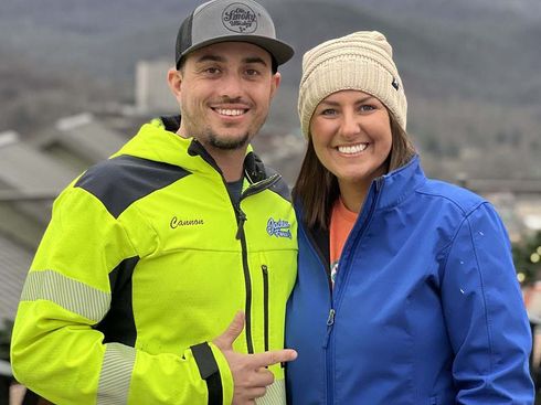 Two smiling people in bright jackets and hats standing outdoors near a roadway