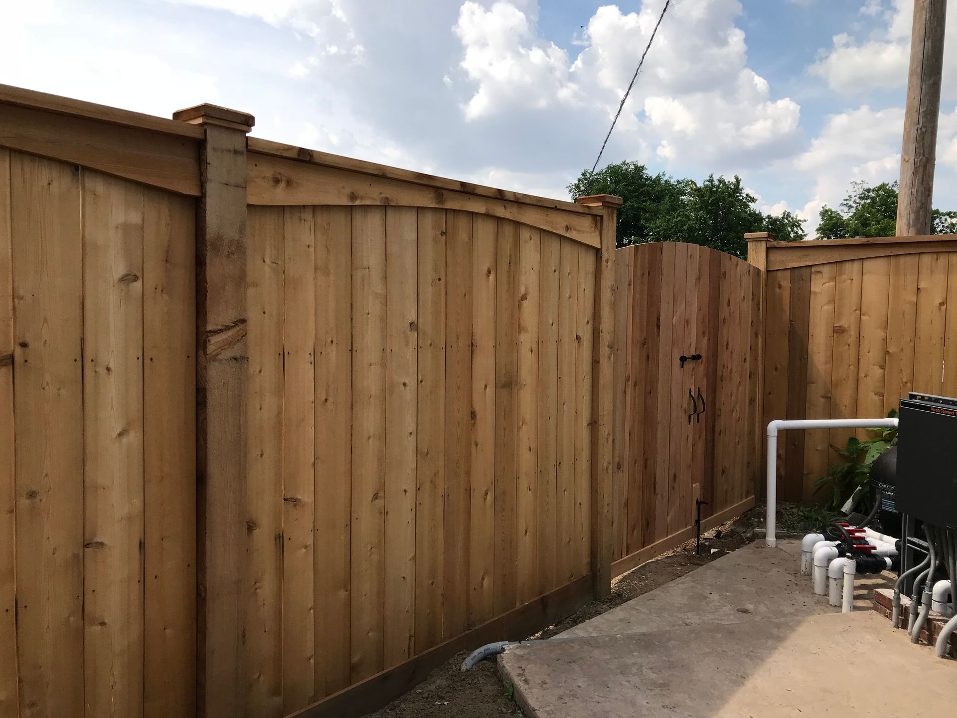 Wooden privacy fence along a narrow backyard patio beside a utility unit and chairs