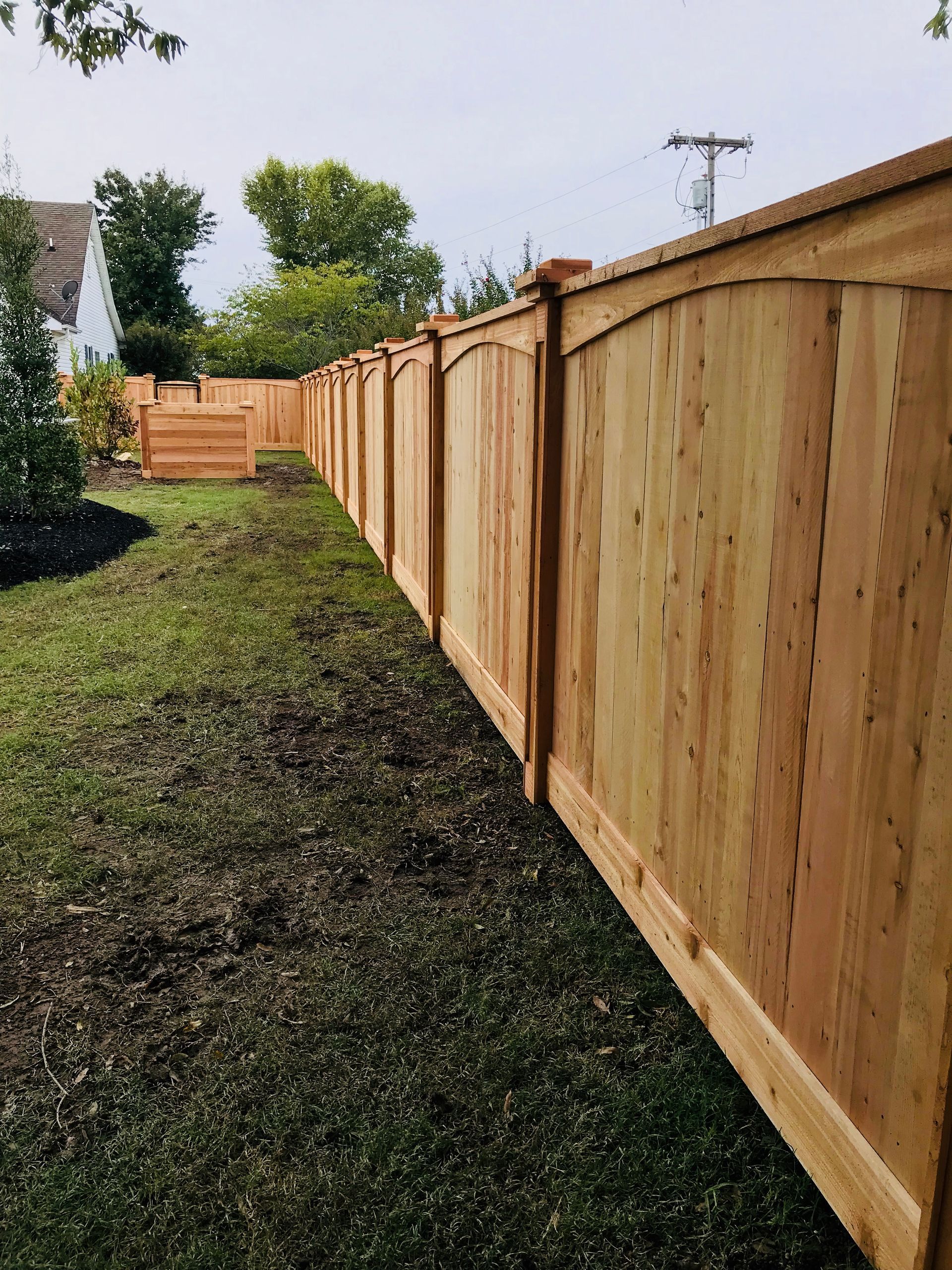 New wooden privacy fence lining a grassy backyard beside neighboring houses