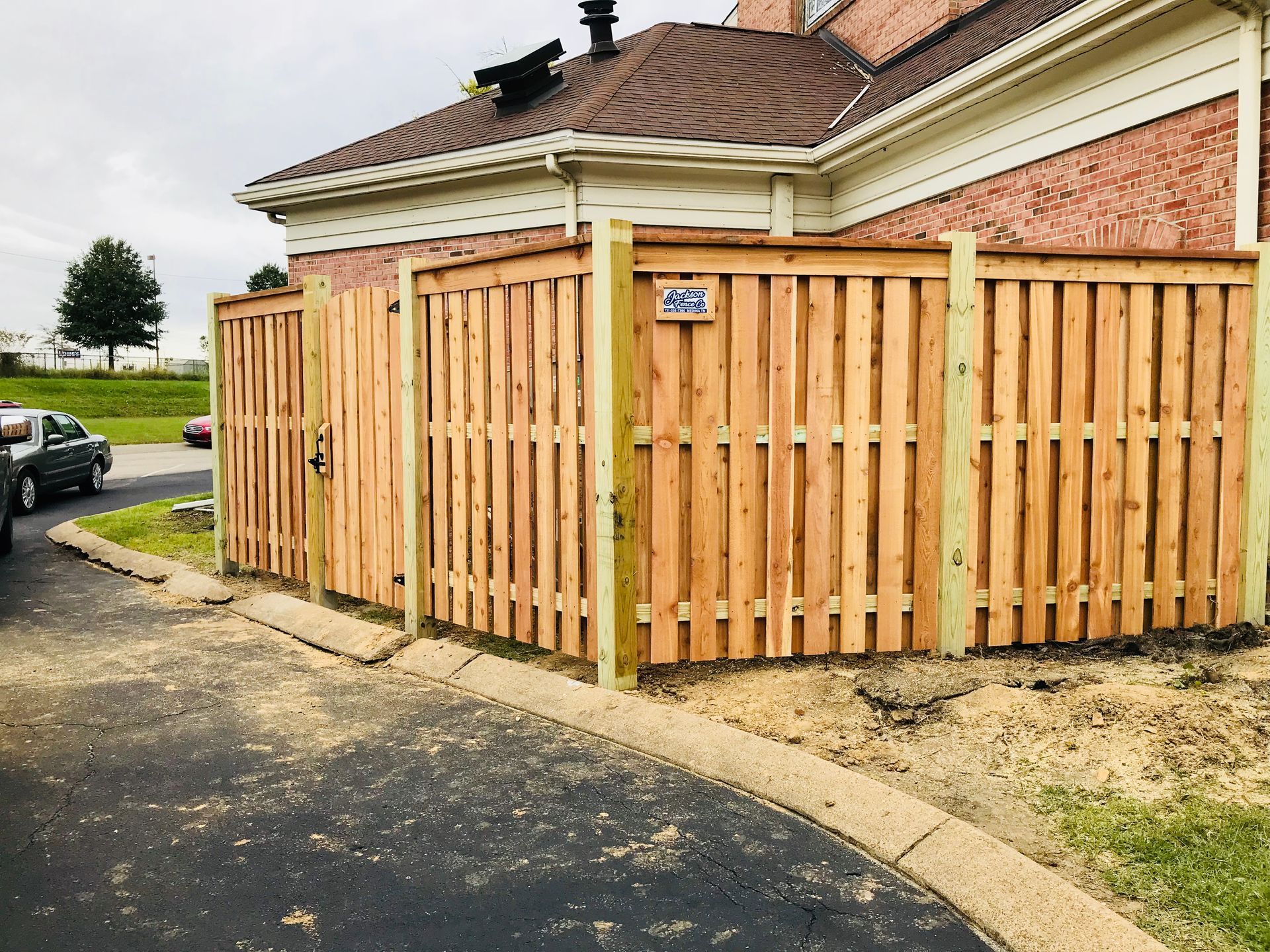 Wooden fence around a brick house corner beside a curved sidewalk and driveway