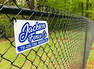 Jackson Fence Co. sign on a chain-link fence near a wooded area