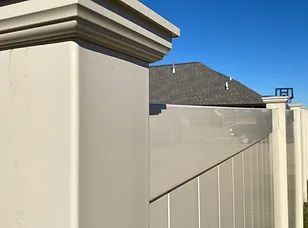 Close-up of a beige fence and post against a clear blue sky, with a dark roof visible behind it
