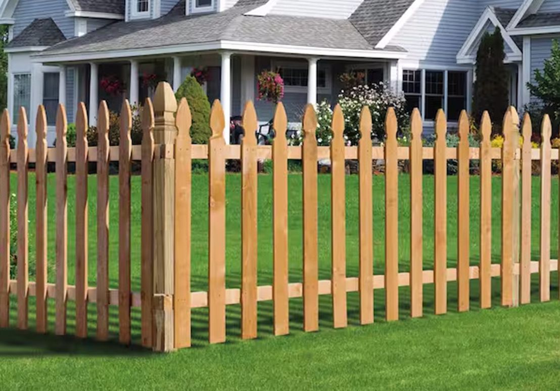 Wooden picket fence with pointed posts in a green suburban yard, with houses in the background