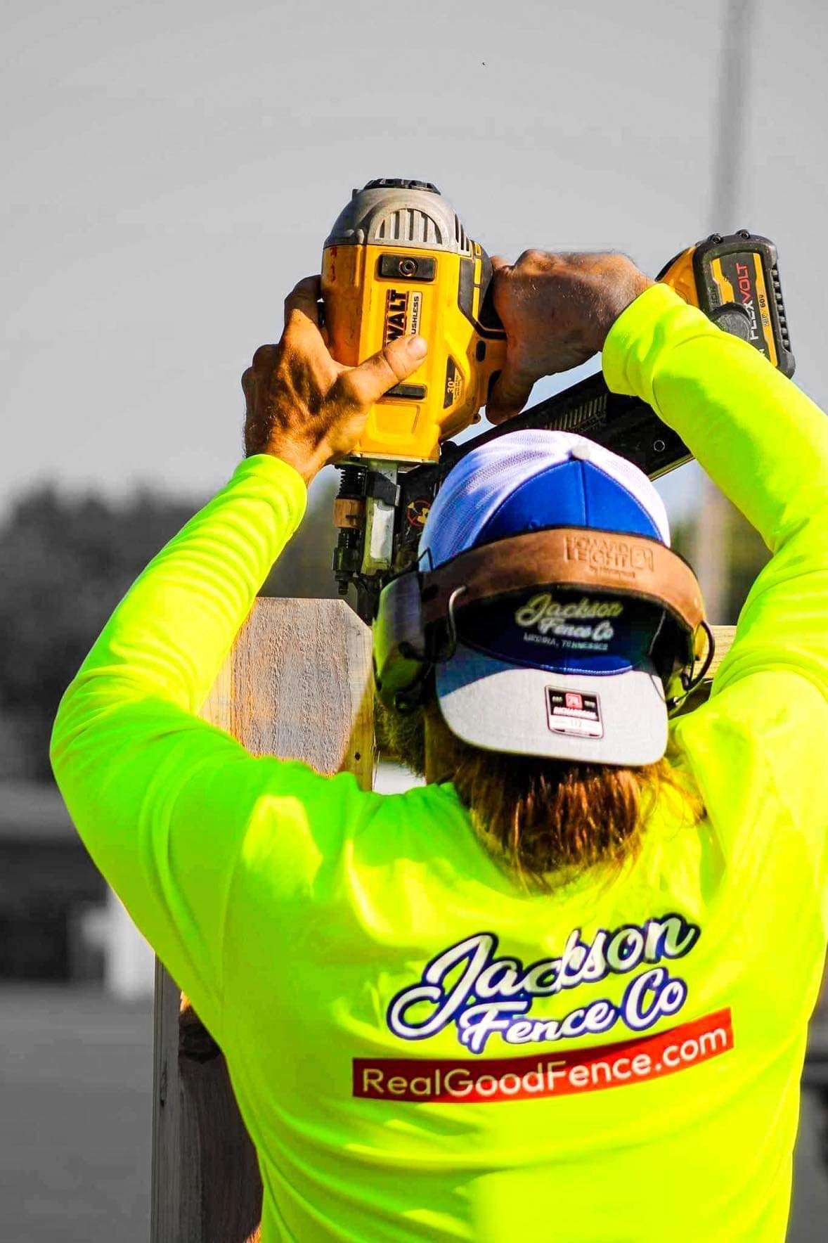 Construction worker using a yellow power drill overhead, wearing neon safety shirt and hard hat.