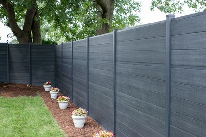 Gray backyard fence with potted flowers along a mulch border beside a grassy lawn