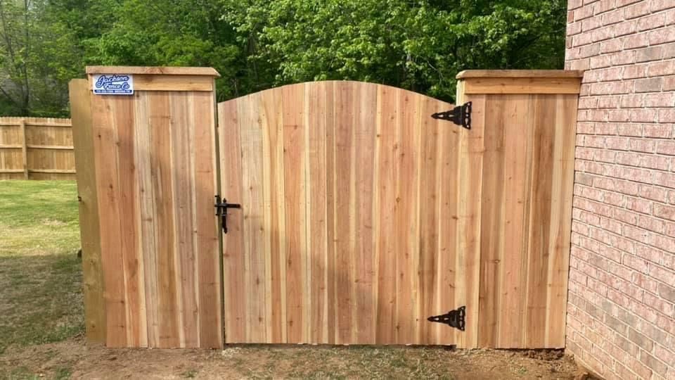 Wooden garden gate with arched center panels between brick walls, set in a grassy yard.