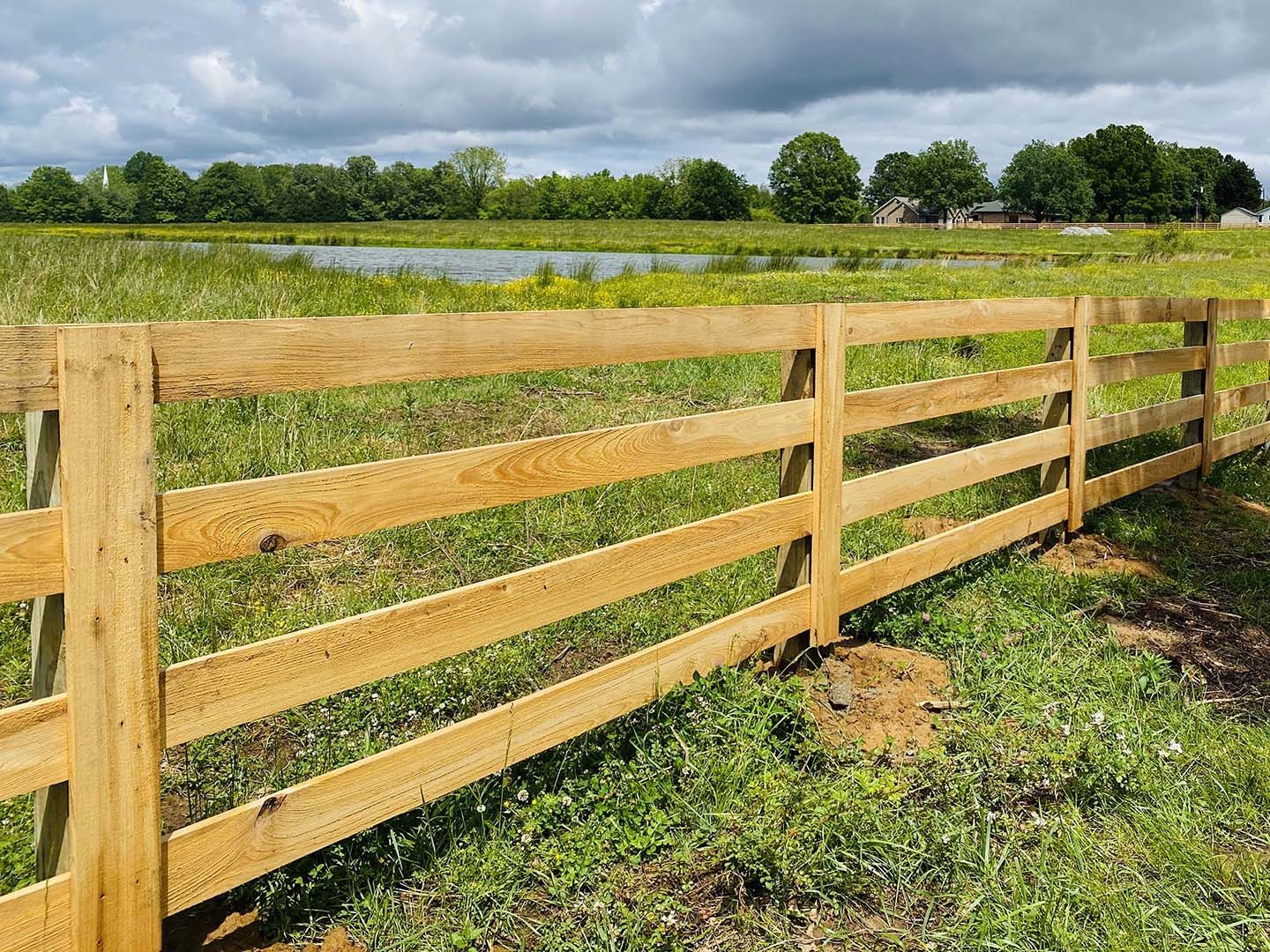 Wooden fence beside a grassy field under a cloudy sky