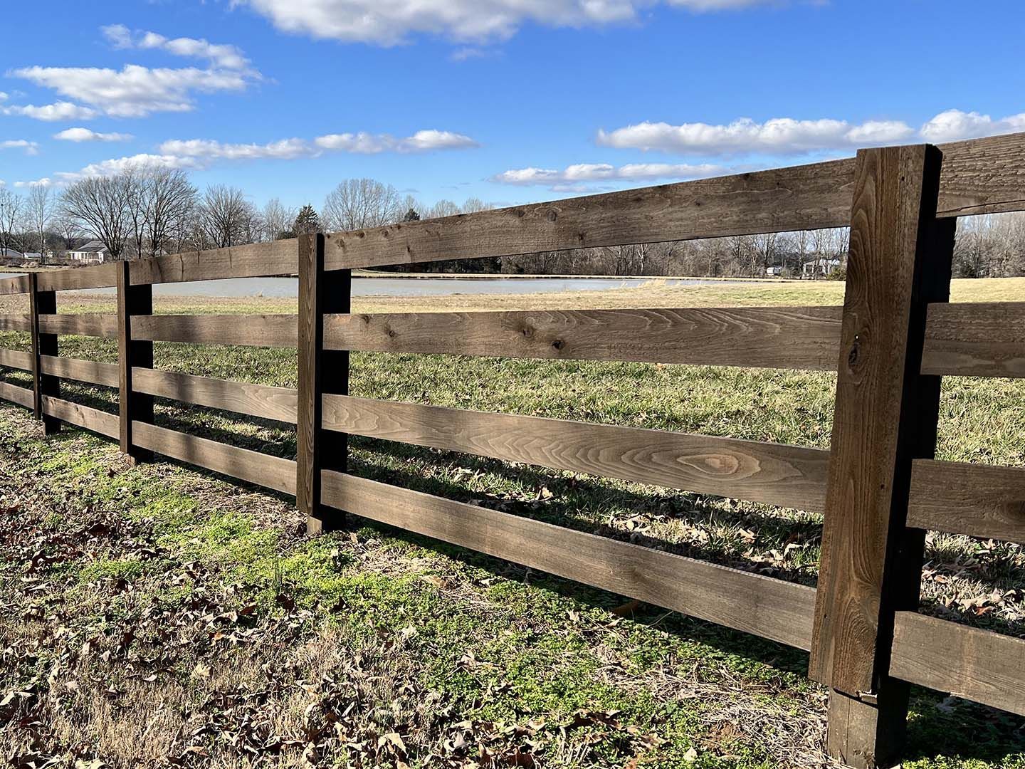Wooden fence bordering a grassy field under a blue sky with bare trees