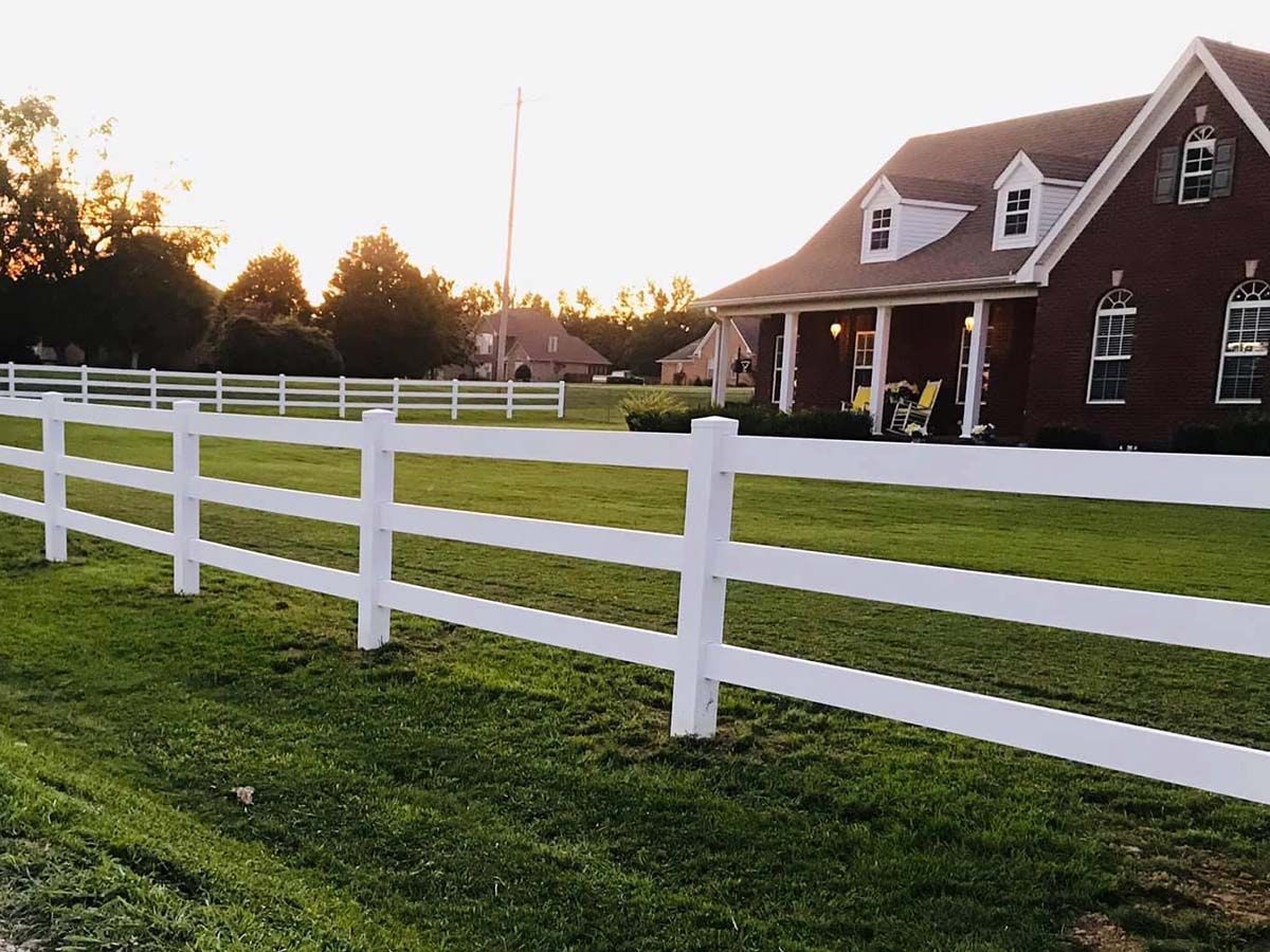 White fence in front of a red brick house at sunset with a green lawn