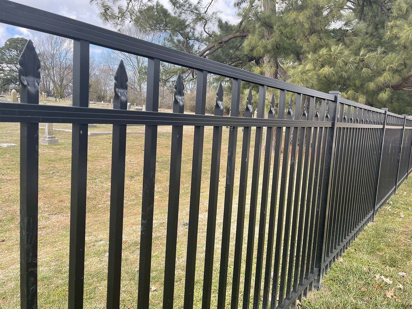 Black metal fence along a grassy yard with trees in the background
