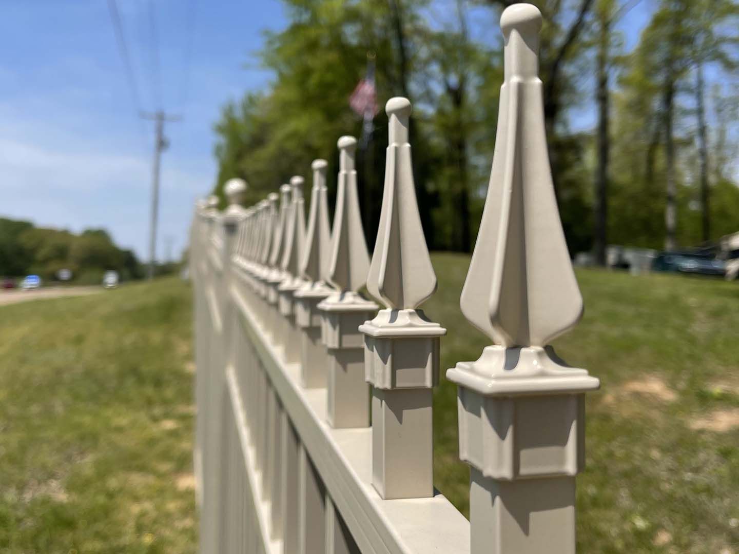 White decorative fence posts along a grassy roadside with trees and blue sky in the background