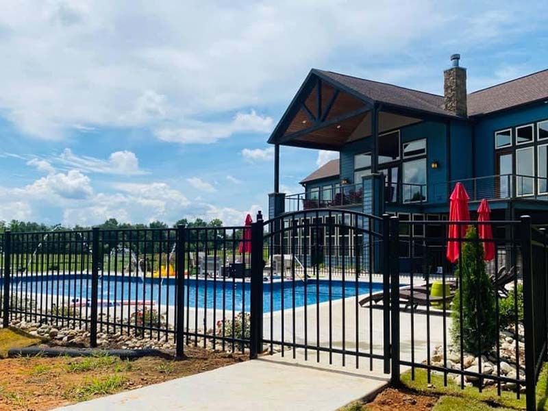 Backyard pool beside a black fence and modern house under a blue sky