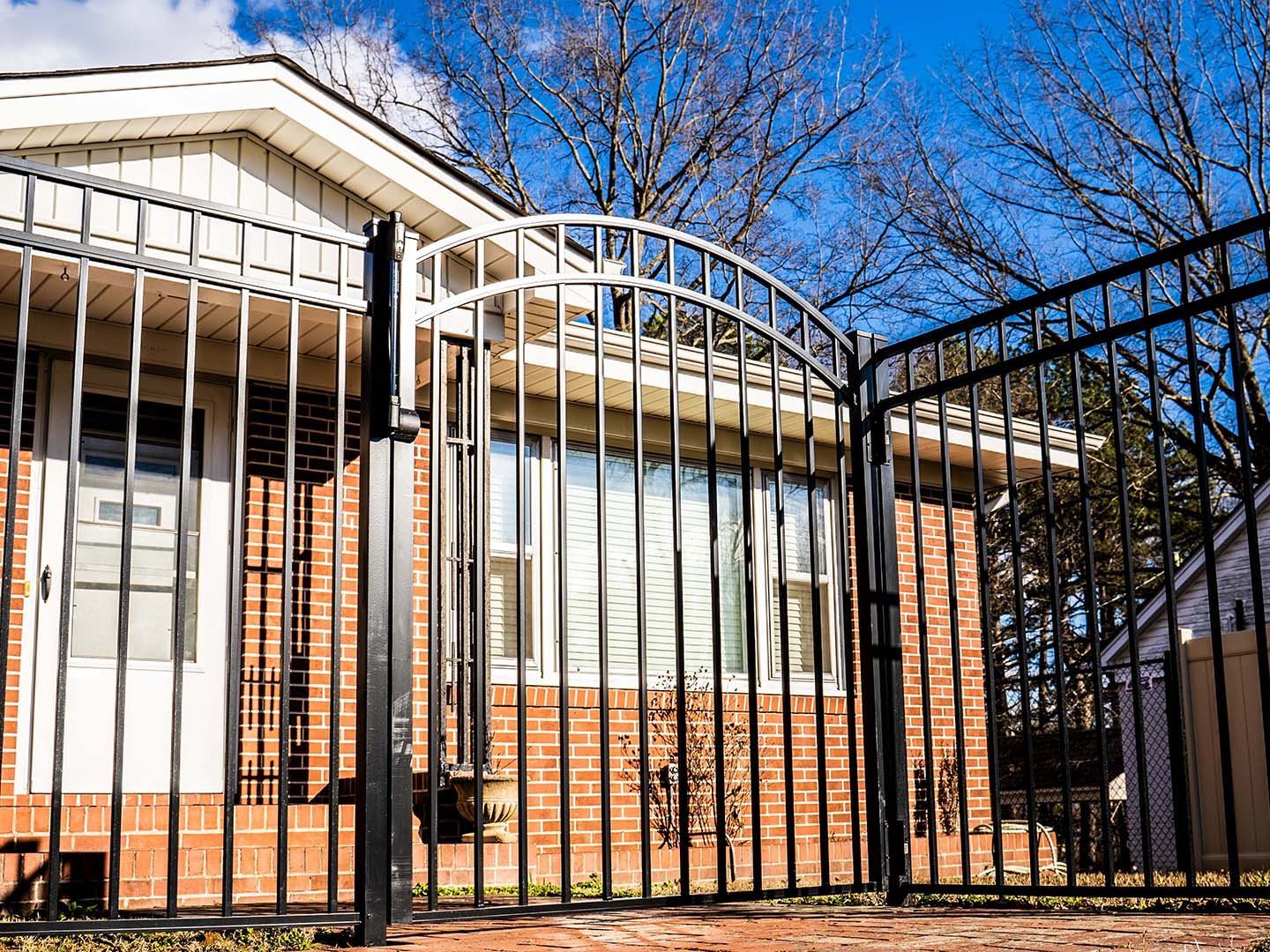 Brick house behind black metal fence under clear blue sky