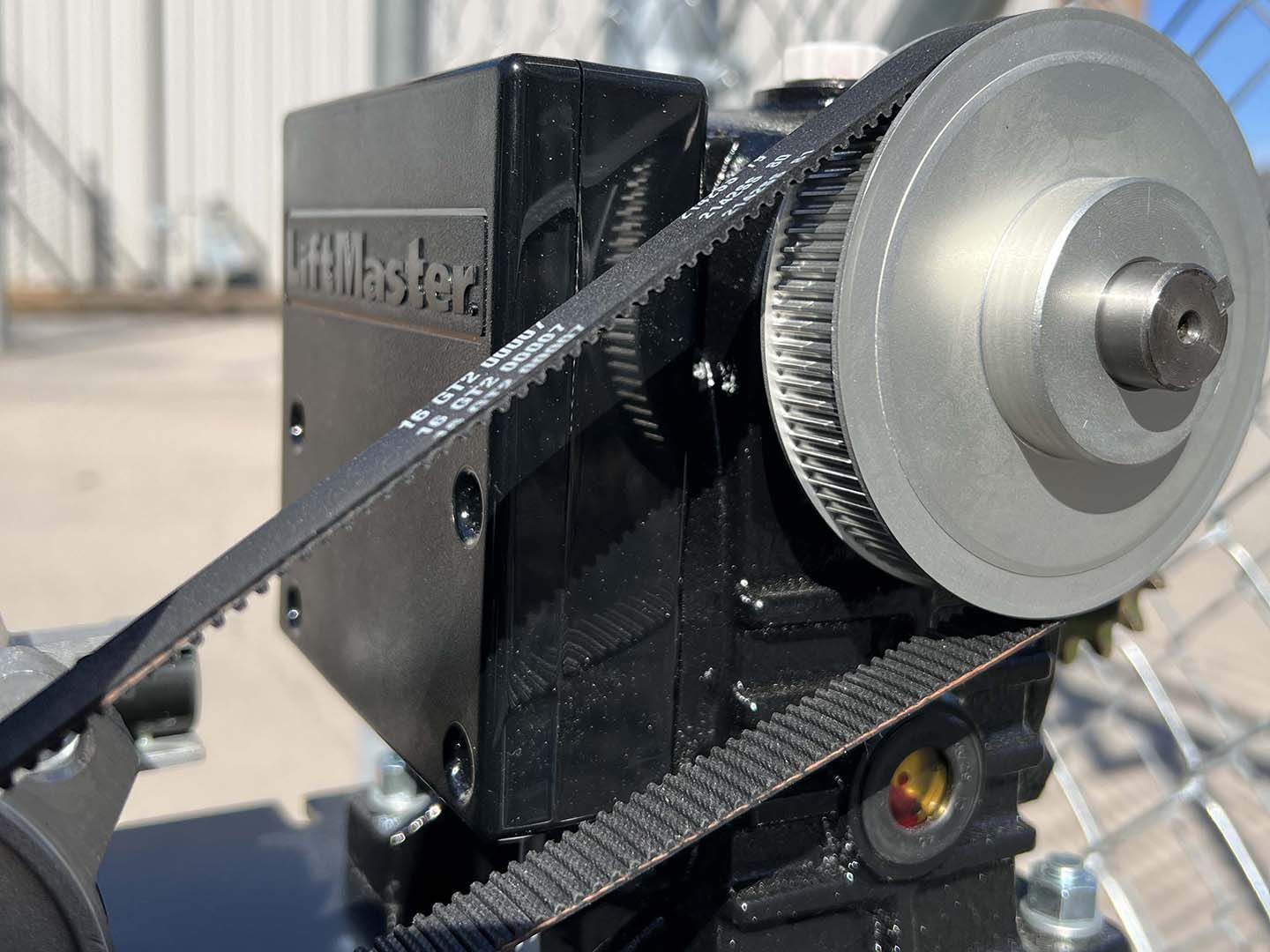 Close-up of a black belt-driven machine with a silver pulley and textured wheels outdoors.
