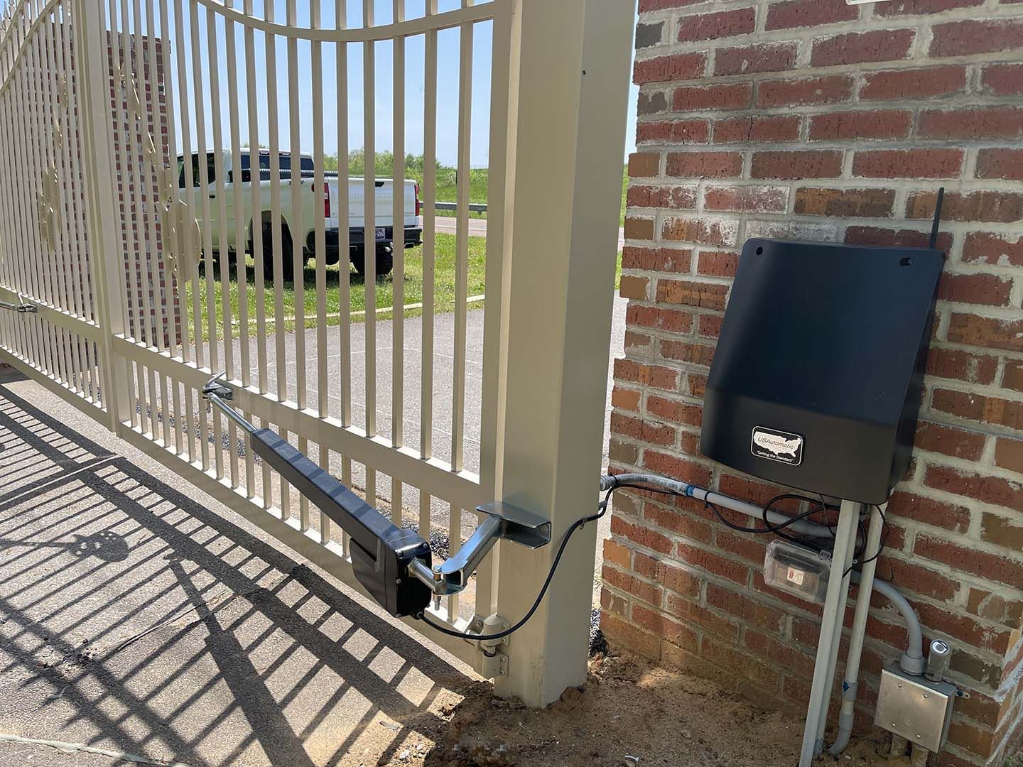 Closed metal gate with a wheelchair attached to it, beside a brick wall and gate opener box