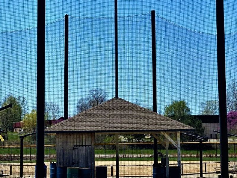 Open-air pavilion in front of a blue netted fence on a baseball field