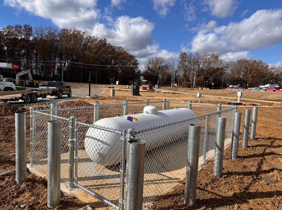 White propane tank in fenced dirt lot under a cloudy blue sky