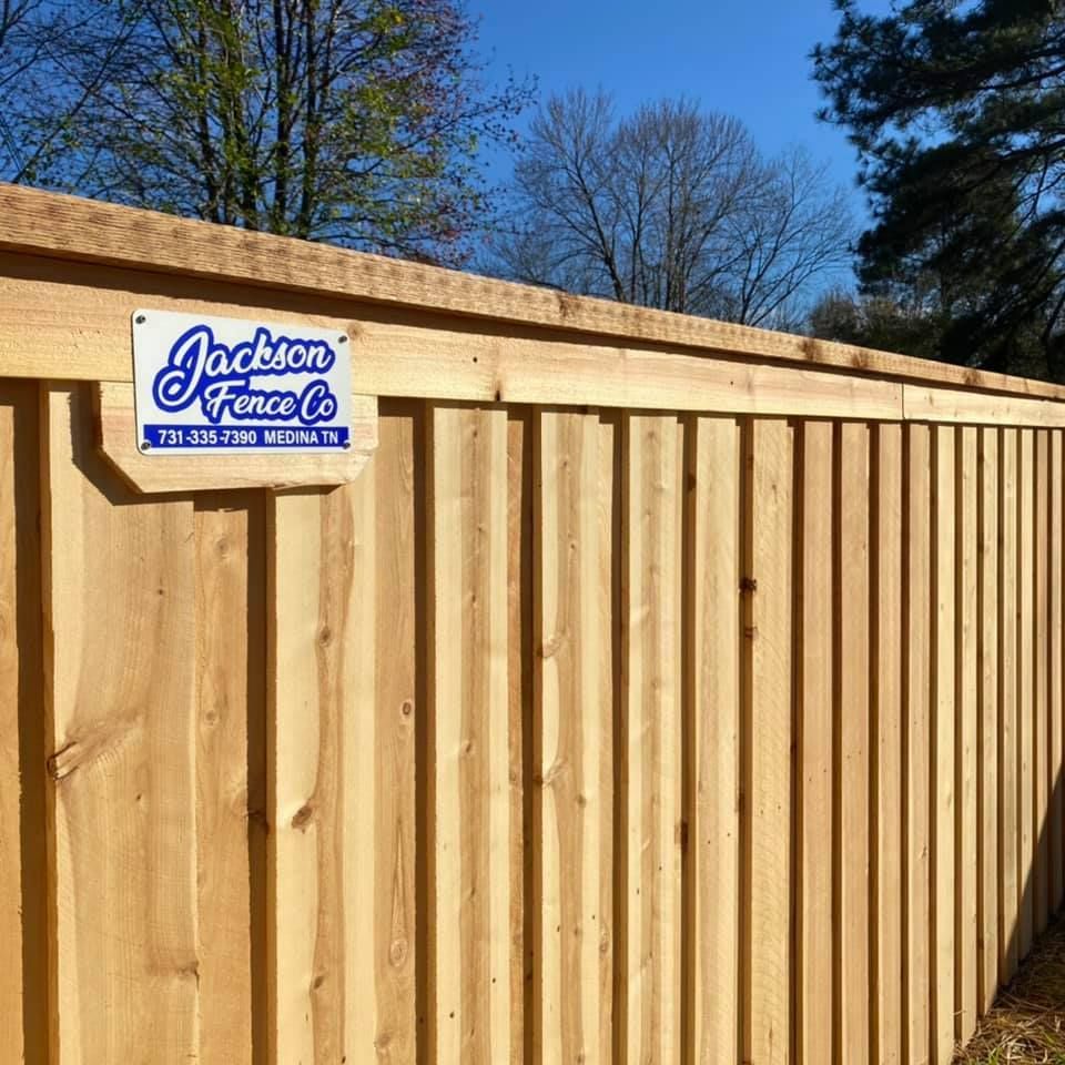 Wooden privacy fence with a blue Jackson Fence Co. sign on the left, outdoors under clear sky