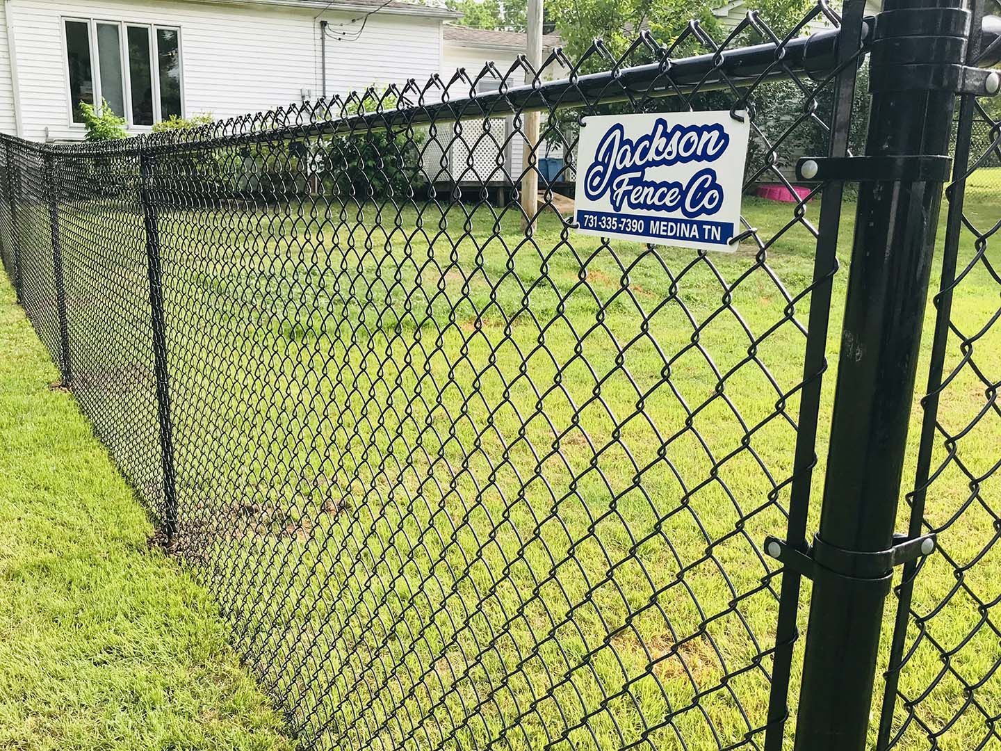Black chain-link fence with a Jackson fence company sign in a grassy yard beside a house