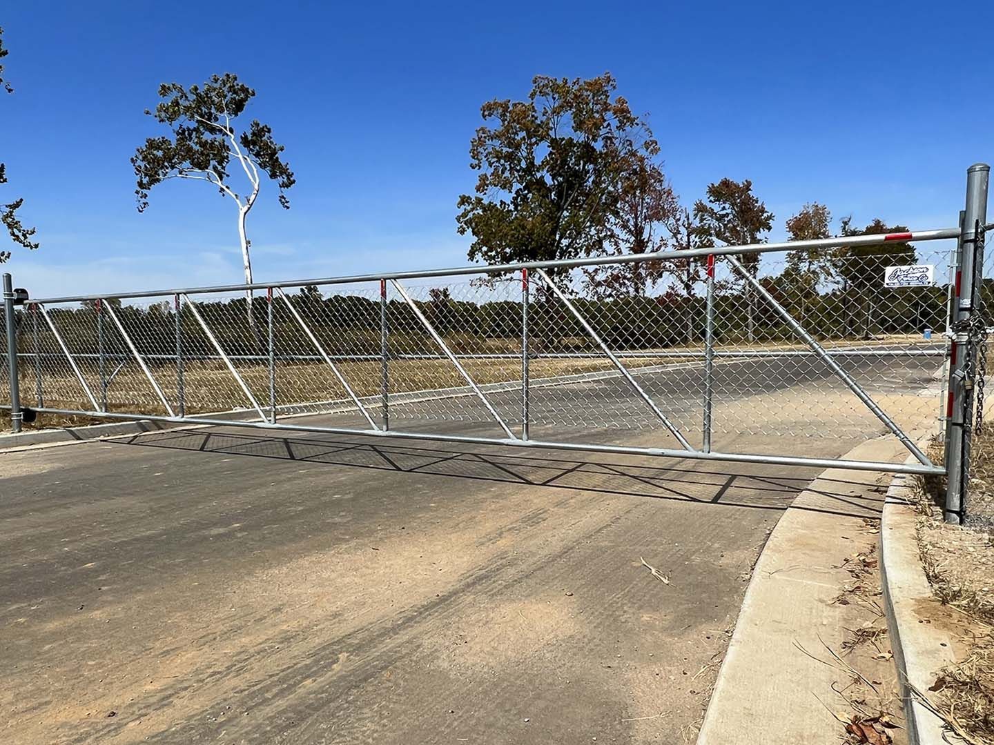 Closed metal gate blocking a paved entrance beside a chain-link fence on a sunny day