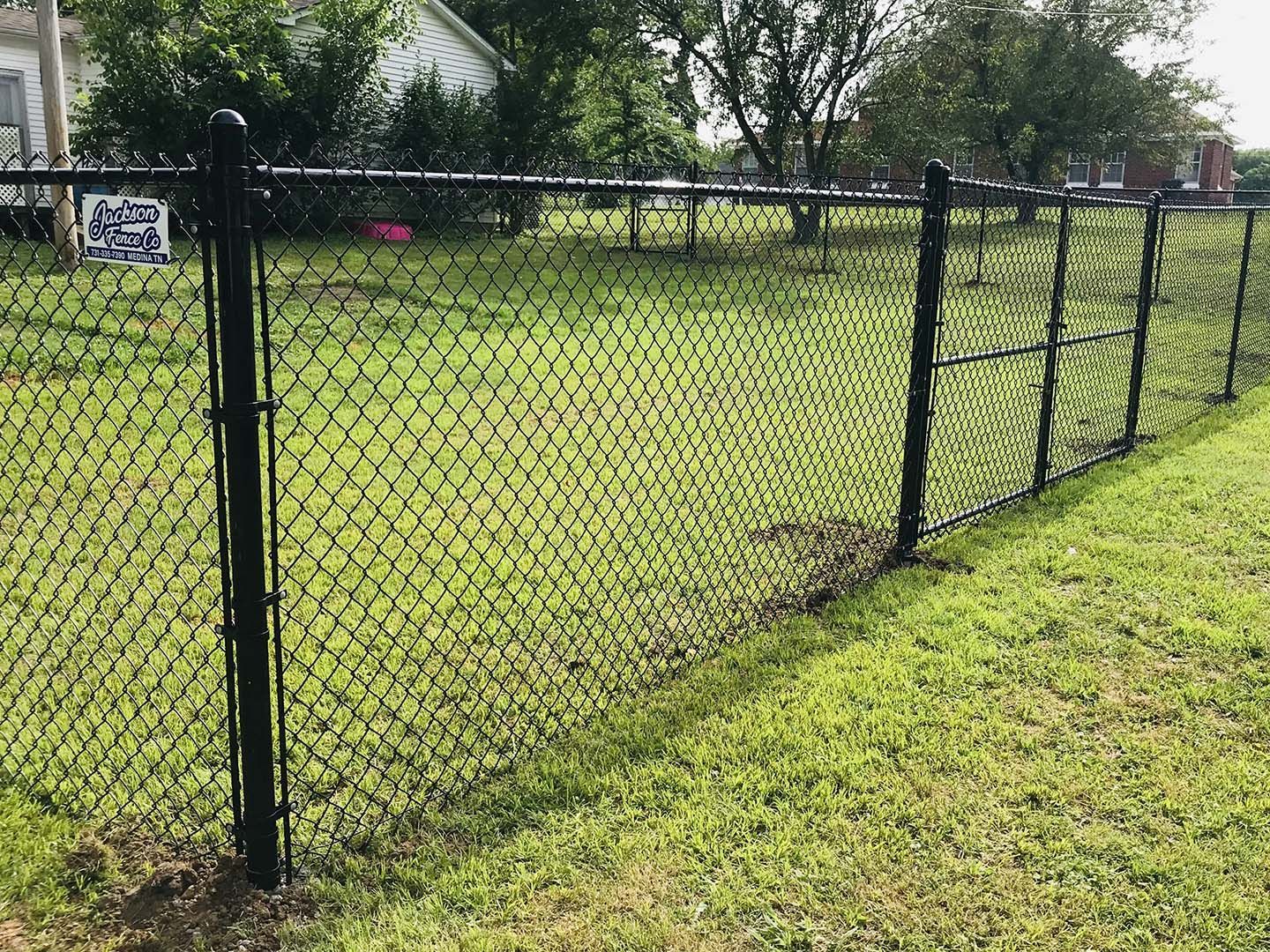 Black chain-link fence along a grassy yard with houses and trees in the background