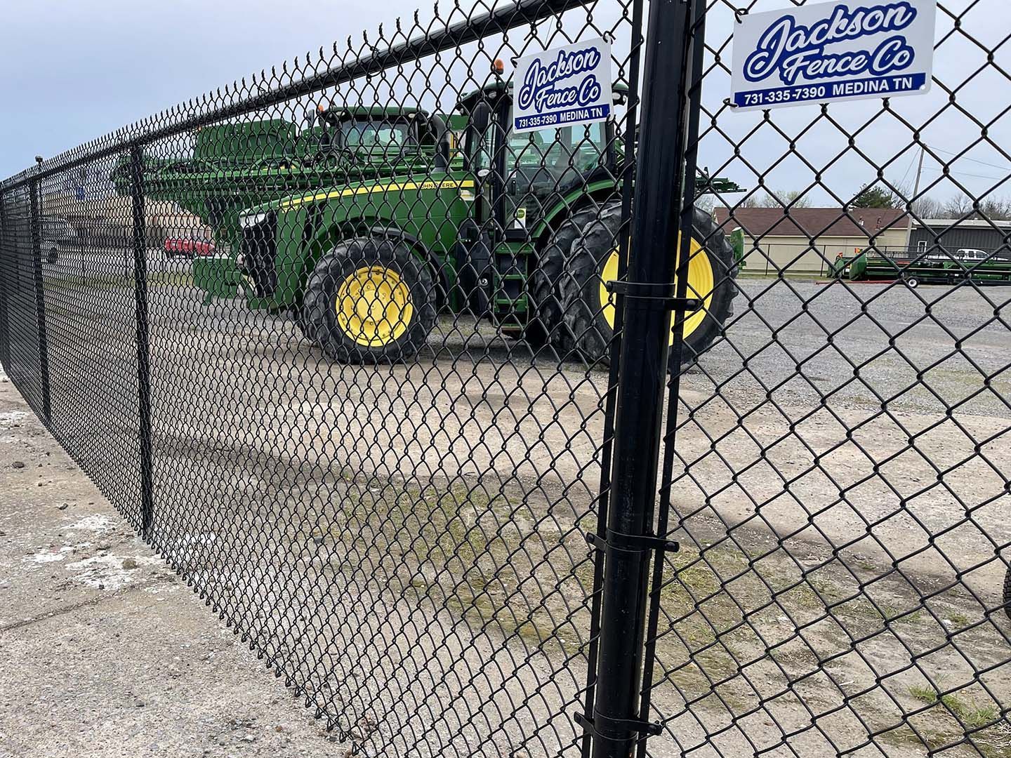 Green tractor behind chain-link fence in a parking lot with a company sign on the cab