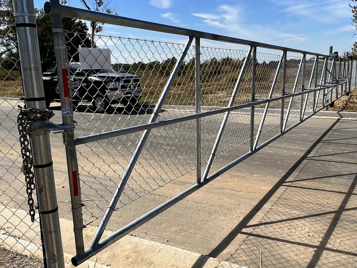 Chain-link sliding gate blocking a paved driveway, with diagonal braces and a vehicle behind it under a blue sky