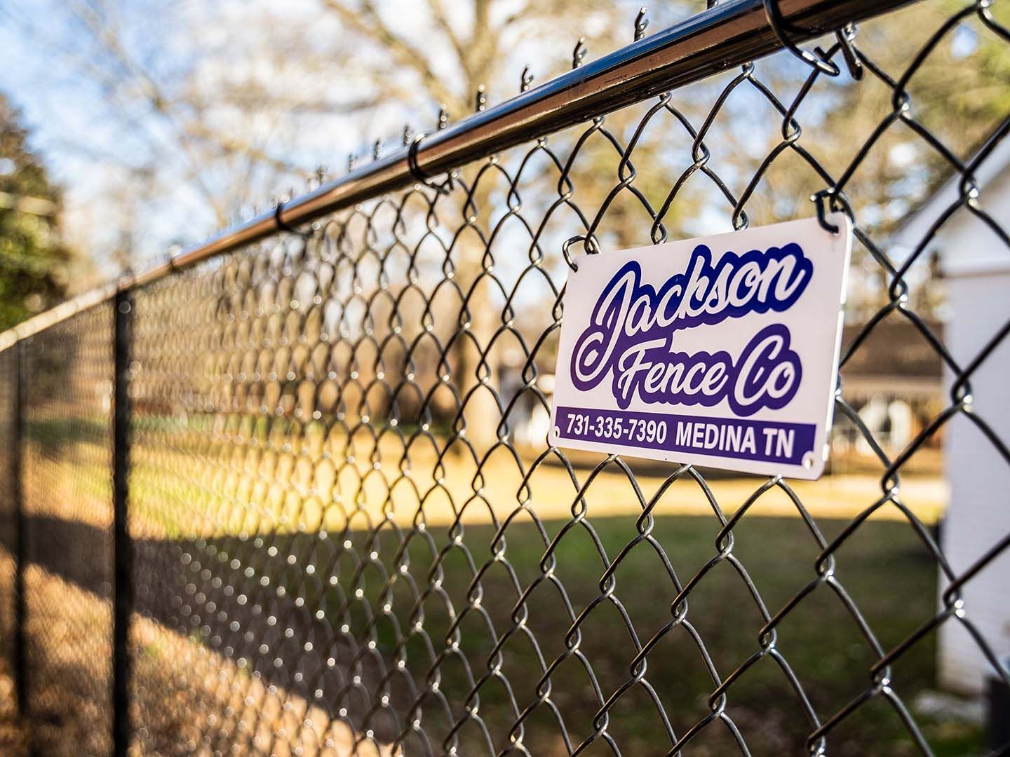 Fence mesh with a Jackson Fence Co sign outdoors by a road.