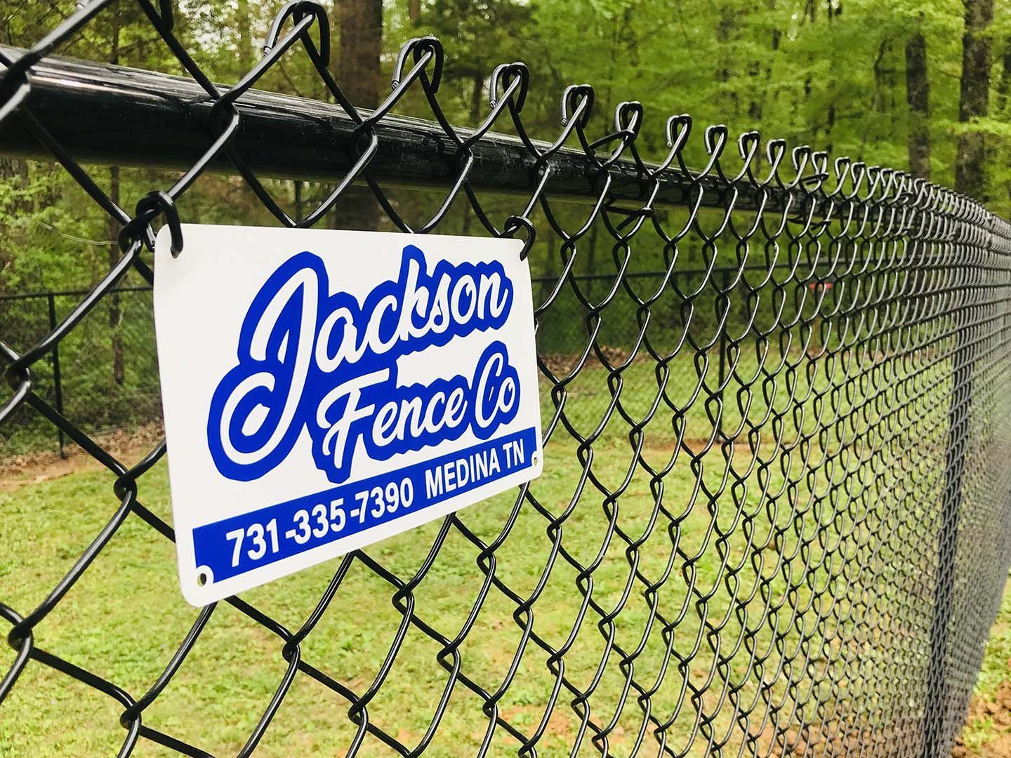 Jackson Fence Co. sign on a chain-link fence beside a grassy path
