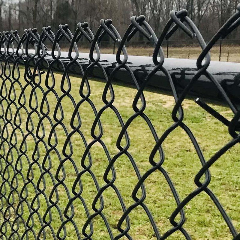 Close-up of a black chain-link fence with a grassy field and road in the background