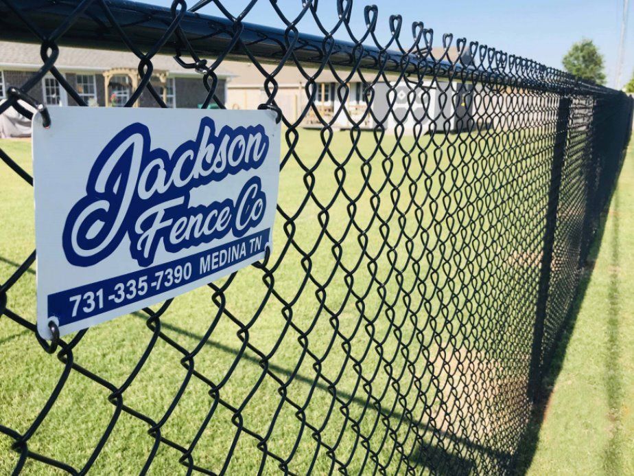 Blue Jackson Fence Co. sign on a chain-link fence beside a grassy field